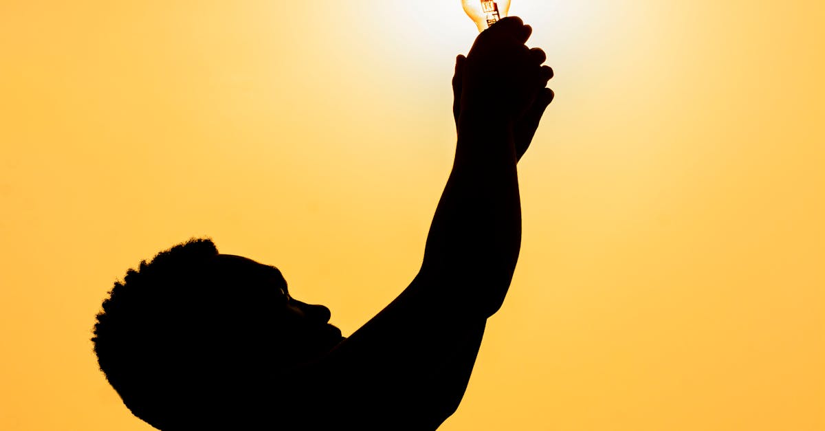 Side view of silhouette of faceless male holding light bulb against bright sun at dusk
