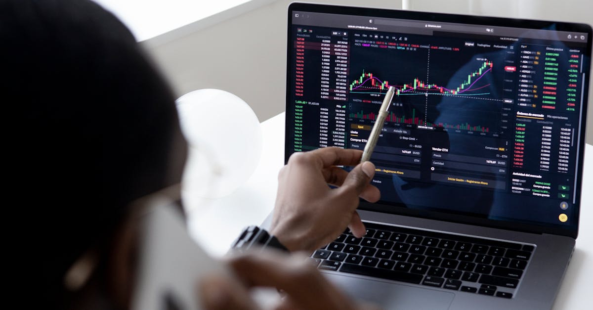 A businessman using a smartphone while analyzing stock market graphs on a laptop indoors.